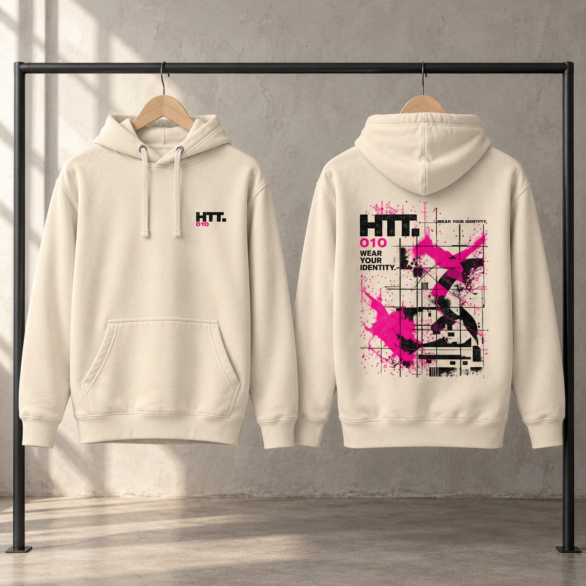 Voor- en achterkant van de crèmekleurige HTT.010 hoodie op houten hangers, met klein borstlogo en zwart-roze rugprint.