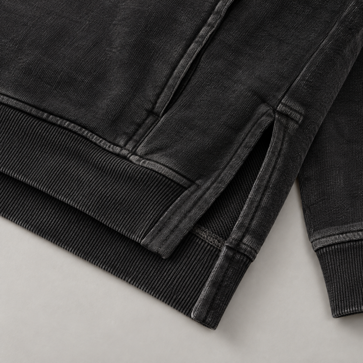 Detail des gewaschenen schwarzen Stoffes, des gerippten Saums und der Konstruktion mit geschlitztem Saum am Hoodie von HTT Blanks