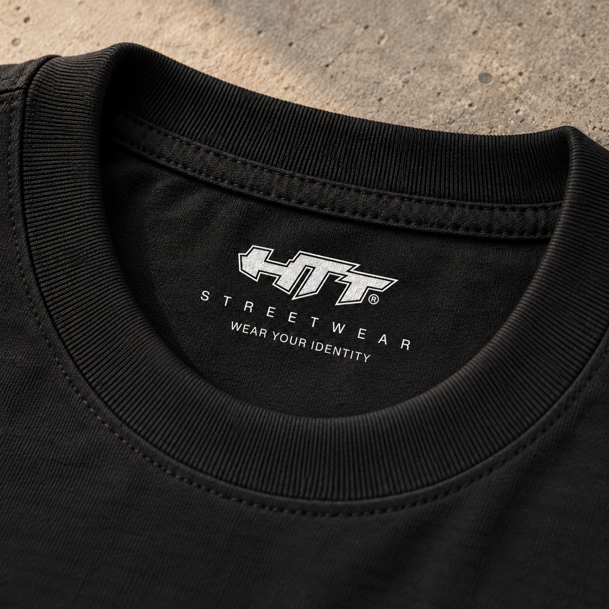 Detail van de ribboord, zwarte katoenen stof en witte HTT Streetwear-nekprint met Wear Your Identity van het Industrial World T-shirt.